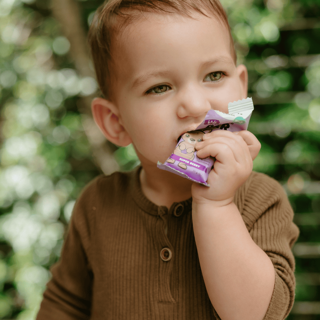 Toddler eating a Sprout Organic Super Berry plant-based bar outdoors