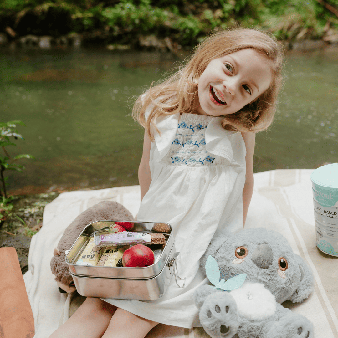 Young girl on a outdoor picnic with lunchbox containing Sprout Organic snack bars.