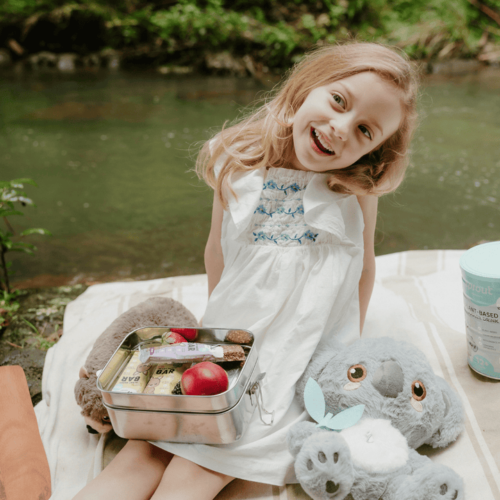 Young girl on a outdoor picnic with lunchbox containing Sprout Organic snack bars.